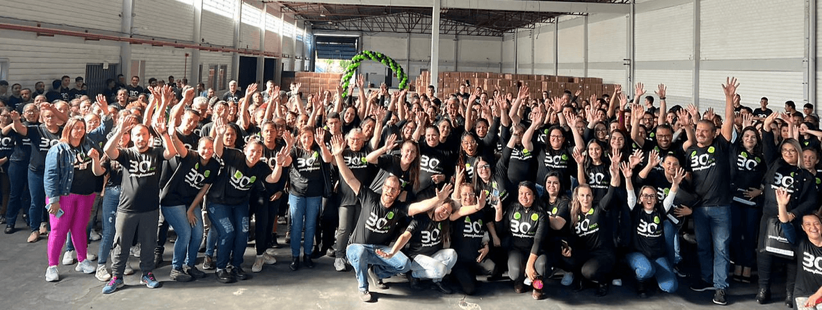 Equipe Pantaneiro reunida em comemoração aos 30 anos, com mãos erguidas em galpão industrial